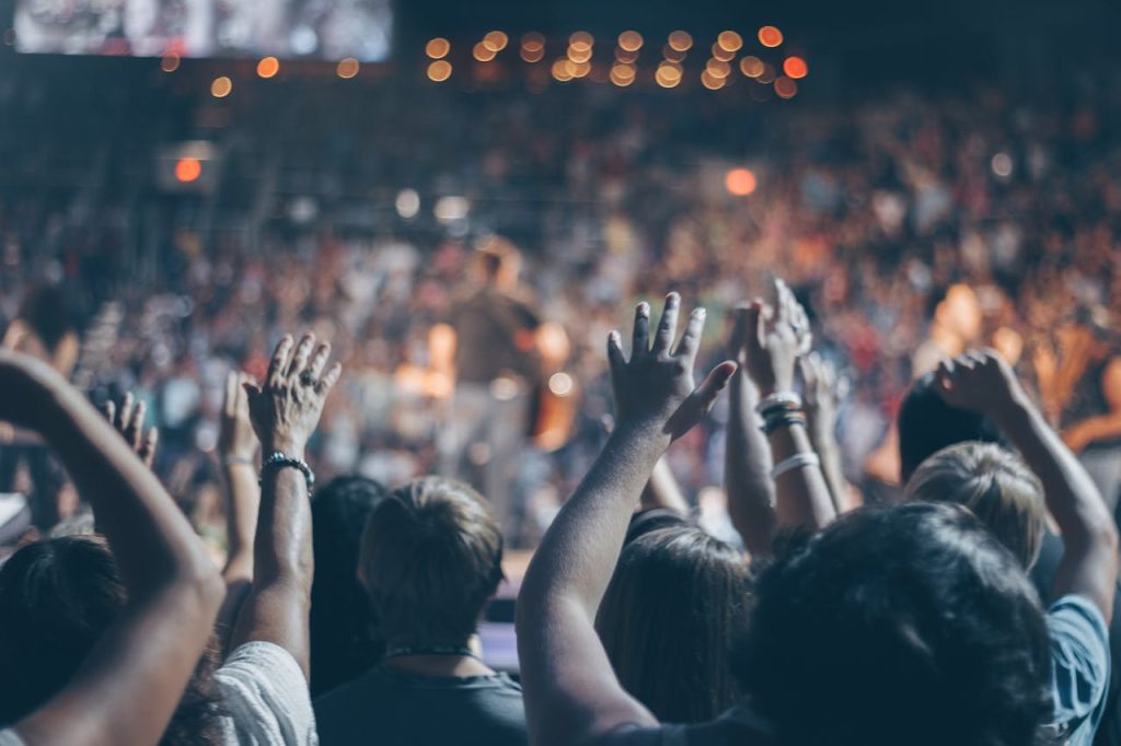group-of-people-raise-their-hands-on-stadium-976866 Energetic crowd at a live concert with hands raised and bright lights.