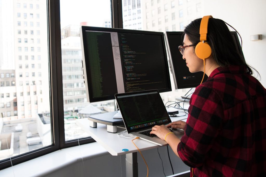 woman-sitting-in-front-laptop-1181677 Woman programming on a laptop at a standing desk in an office with large windows.